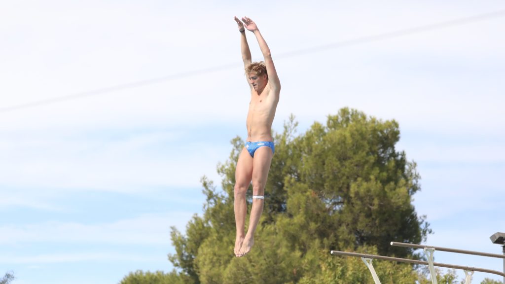 Ben Willett leaps into the air from a diving board with arms raised and eyes trained down.