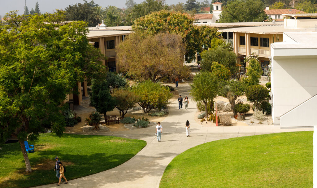 An aerial shot of Pitzer’s campus showing the grassy Mounds, green trees, and white and beige academic buildings as students walk along pathways.