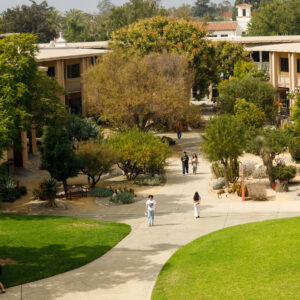 An aerial shot of Pitzer’s campus showing the grassy Mounds, green trees, and white and beige academic buildings as students walk along pathways.
