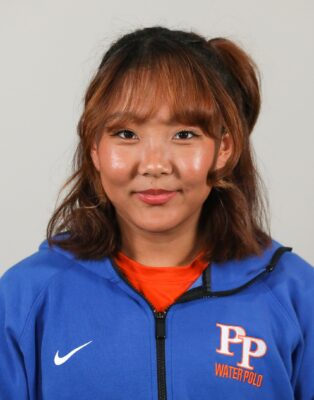 Namlhun Jachung has shoulder-length dark hair with auburn tips and wears and orange shirt under a Pomona-Pitzer blue jacket.
