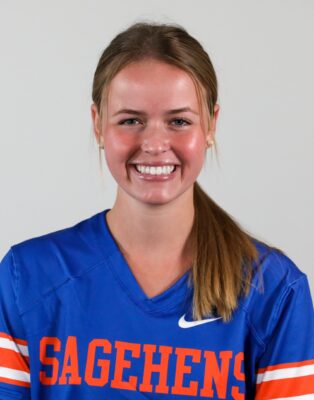 Sydney Landauer has long dark blond air in a ponytail and wears a blue uniform with the word Sagehens in orange text