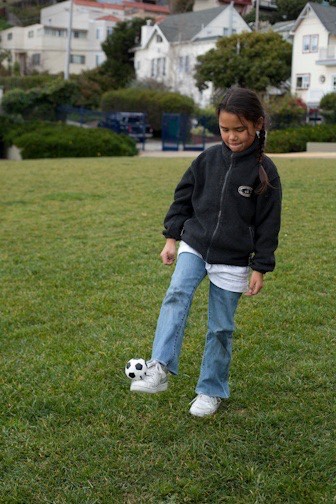Pugh as a child stands in a grass field with a tiny soccer ball balanced on one foot.