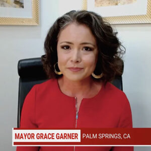 Grace Garner has shoulder-length curly dark hair and wears hoop earings and a red shirt.