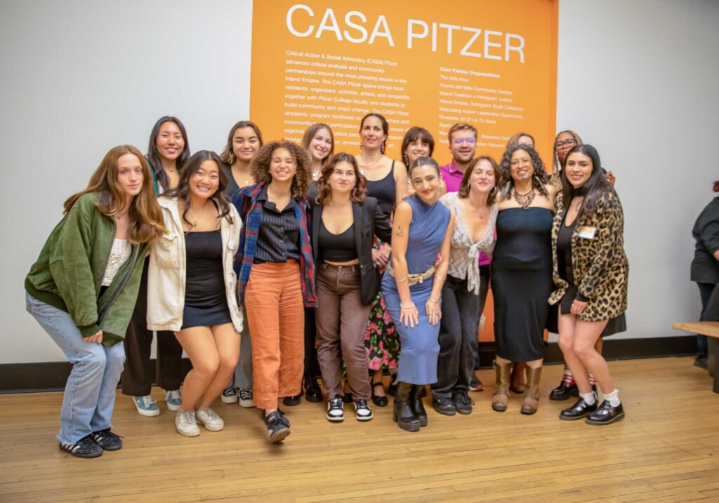 CASA Pitzer students and staff take a group photo in front of an orange wall with CASA Pitzer's name and mission in white text.