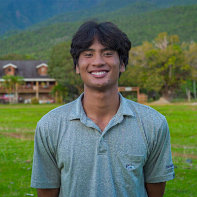A portrait photo of Sammy Basa standing on a field of green grass with rolling green hills in the background. Basa has short dark hair and wears a gray polo shirt. 