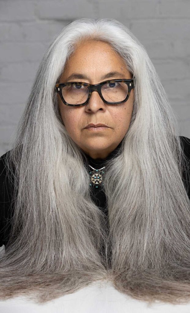 Portrait photo of Laurie Steelink. Steelink has long, straight gray hair and wears a black top and black-rimmed glasses.
