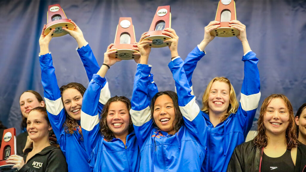 The Pomona-Pitzer women’s swim and dive team smile and hold up the NCAA trophies above their heads.