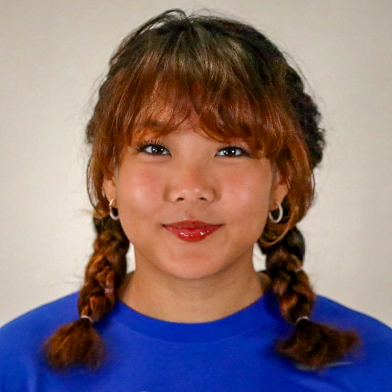 Headshot of Namlhun Jachung. Jachung wears a blue shirt and has dark hair dyed red at the ends and pulled into two braids.