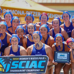 The Pomona-Pitzer women’s water polo gather for a group photo while holding up a sign that reads 2024 Women’s Water Polo SCIAC Tournament Champions.