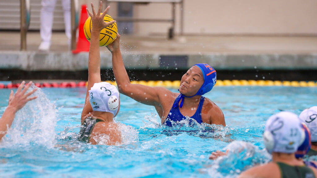 An action shot of Namlhun Jachung in the pool. Another player attempts to block Jachung as Jachung holds up the yellow ball.
