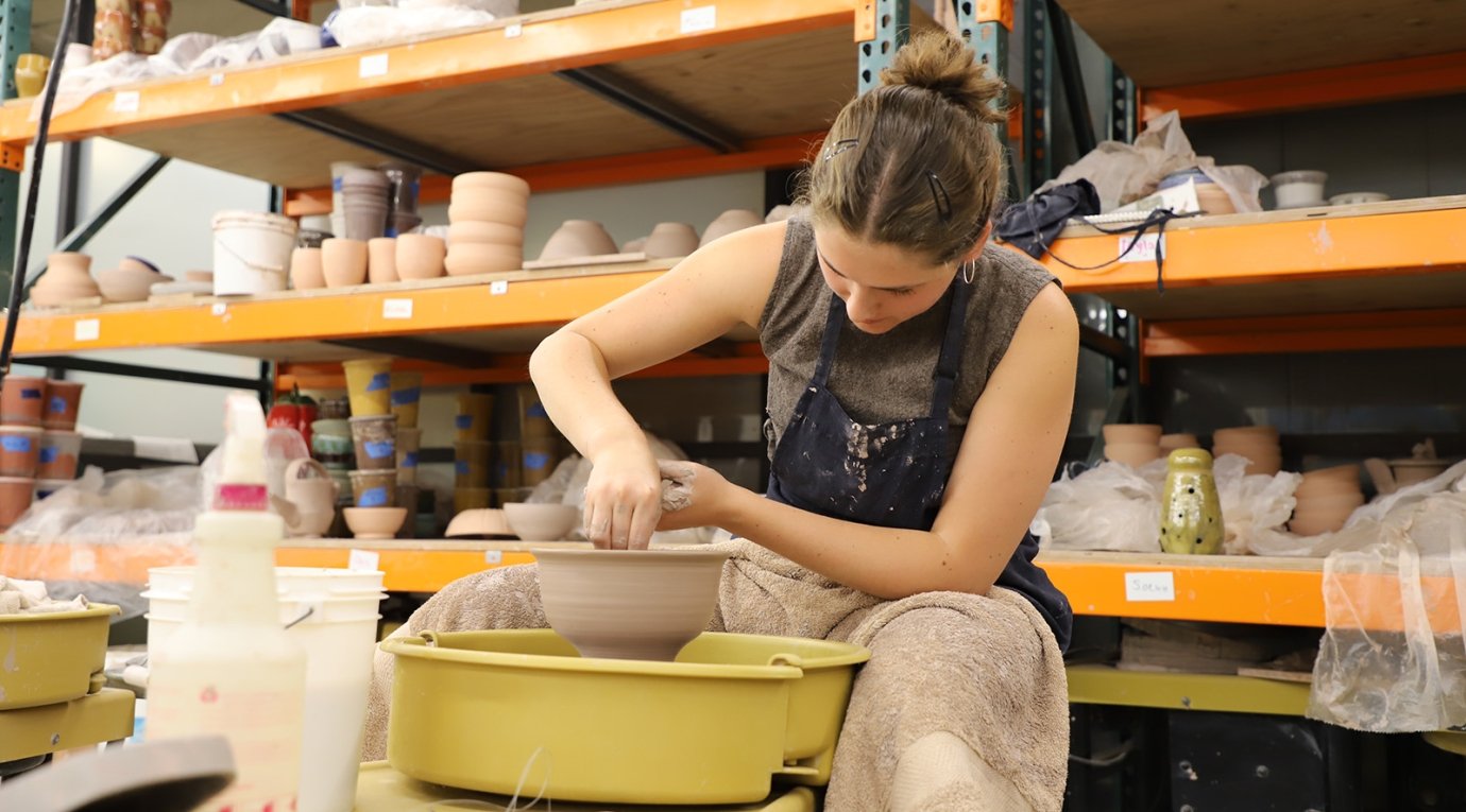 A Pitzer art student works a piece of clay on a wheel