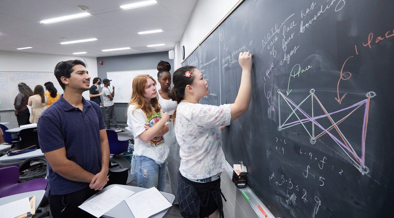 A student works out a math problem on a blackboard