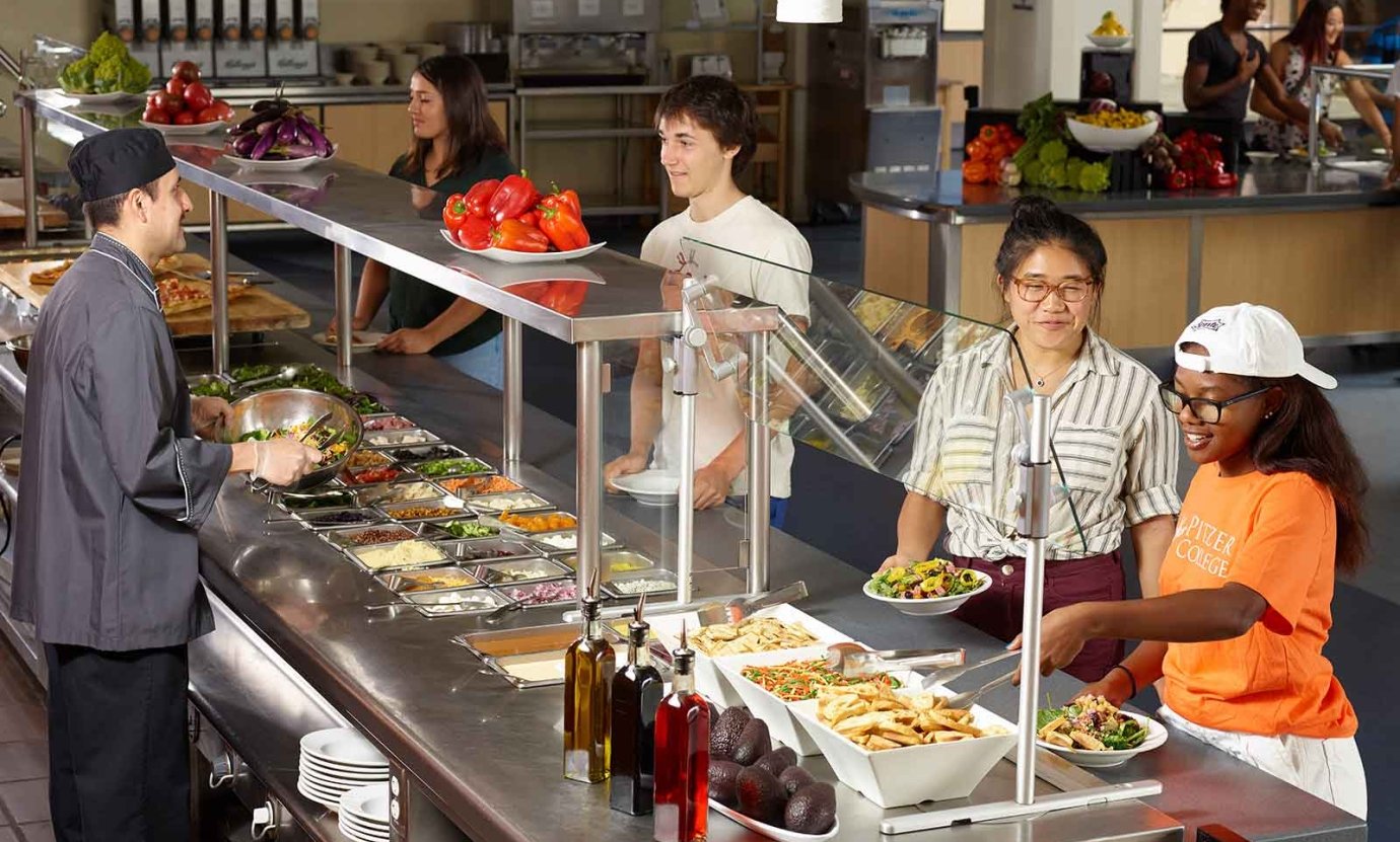 three students get food in the dining hall with a dining hall staff person helping them behind the counter