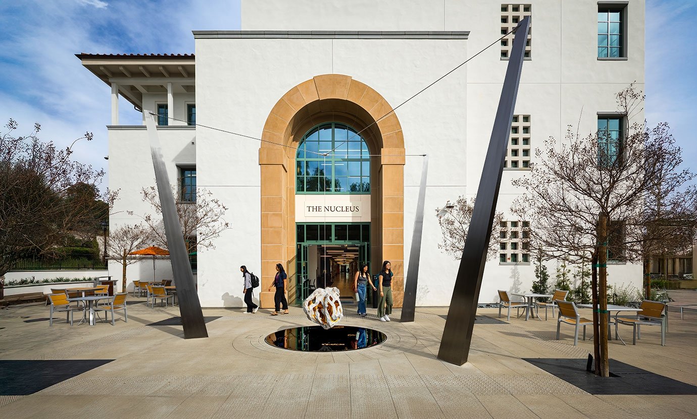 students walk past the arched entrance of the nucleus building on a bright day