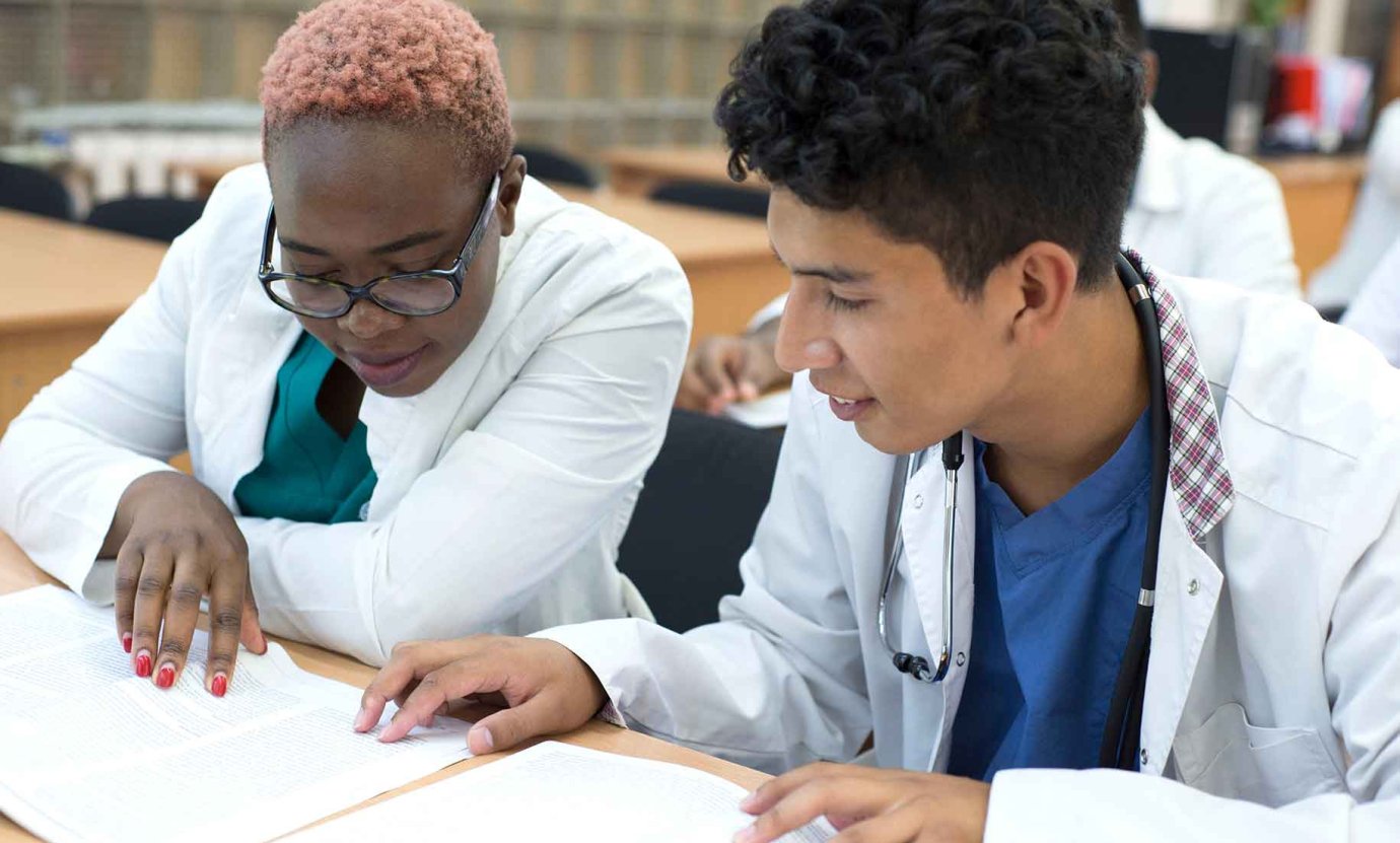 two students in white lab coats study together at a desk