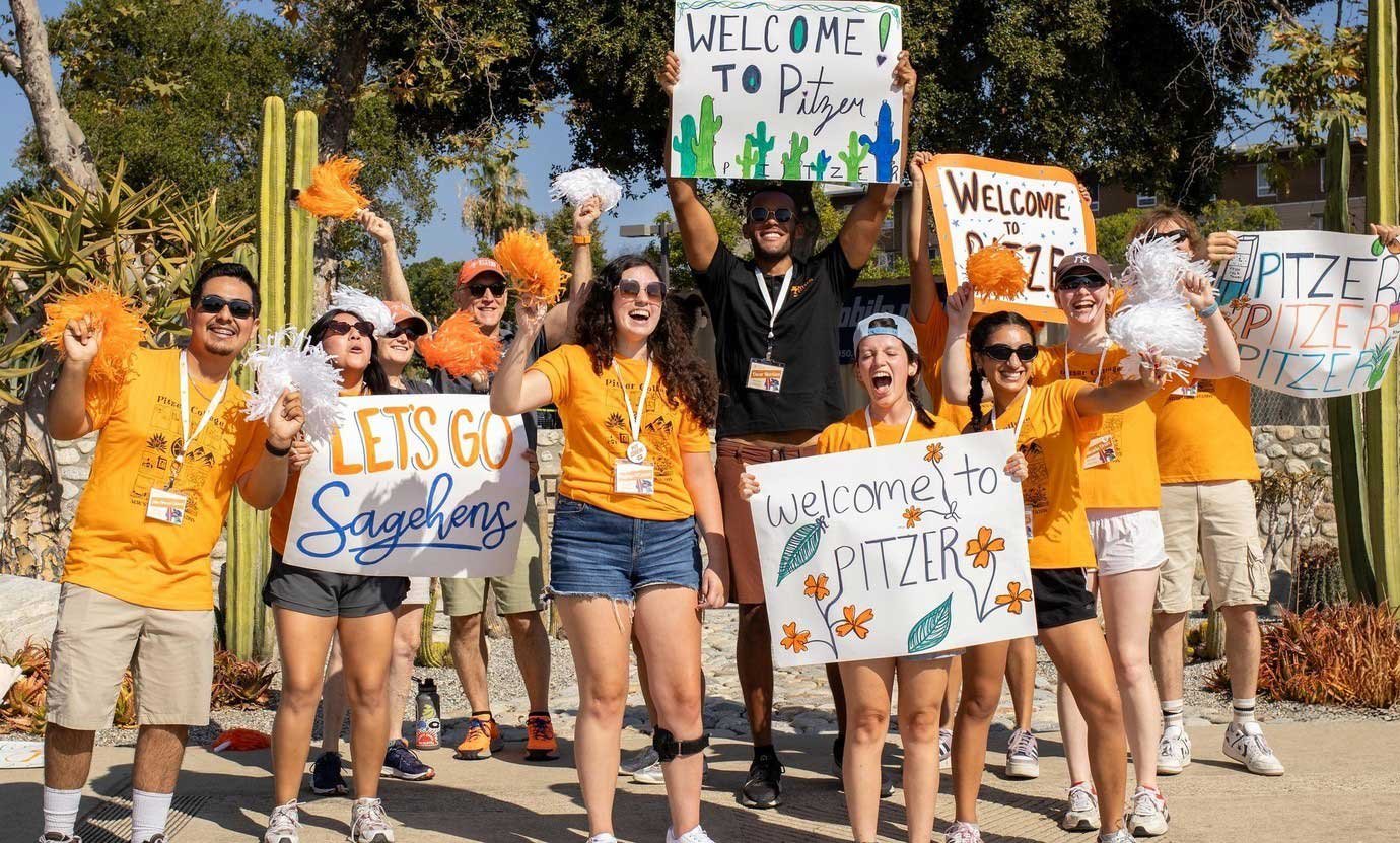 a crowd of students wearing pitzer orange hold up signs welcoming new students to campus
