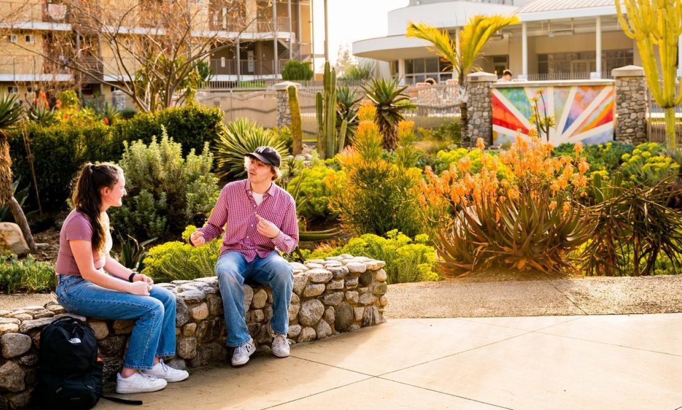 two students sit on a wall conversing near the Pitzer dorms