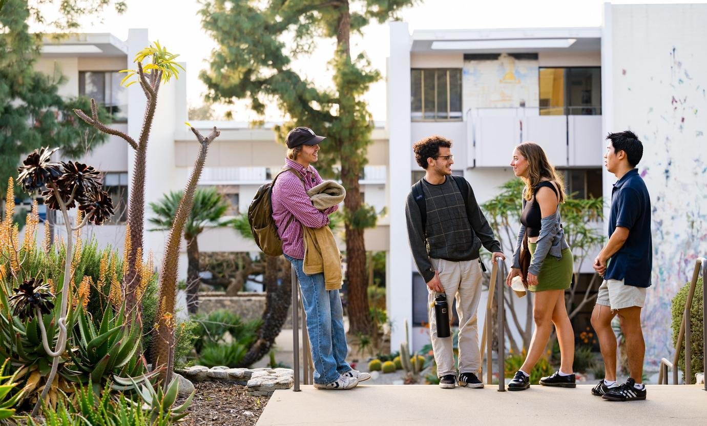 four students chat at the top of stairs in front of mead hall