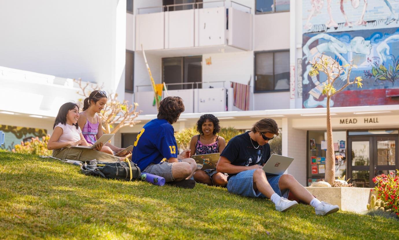 a group of students sit on the grass in front of Mead Hall