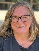 a woman with shoulder-legnth blond hair wears black glasses ad a blue tshirt