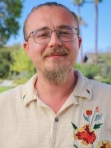 headshot of Tim Lewis wearing a ivory collared shirt embroidered with a colorful flower