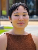 Maria Paz Almenara has close-cropped straight black hair and wears a sleeveless copper top while standing outdoors.