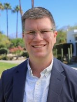 Man wearing navy colored suit with glasses and short brown hair.