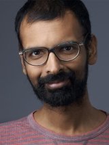 Man with short black hair wearing black glasses and red t-shirt.
