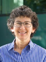 Woman wearing blue striped shirt and glasses with short brown curly hair.
