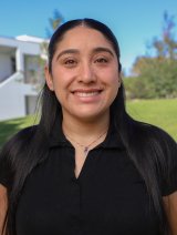 Woman with long black hair wearing black top with necklace.