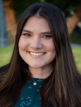 Woman in green floral top with black blazer and long brown hair. 