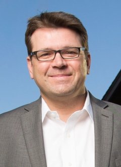 A portrait Jim Marchant wearing glasses, a white shirt and grey jacket