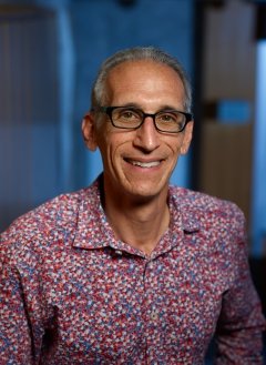 Man, smiling, with gray hair, wearing glasses, and patterned collared shirt.