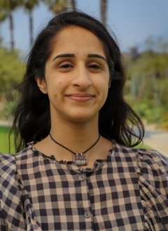 Closeup of Shriya Nagpal, who has long wavy dark hair and wears a black and tan plaid top.