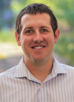 Closeup of Zachary Wilson, who has short dark hair and wears a plaid white and pale blue collared shirt.