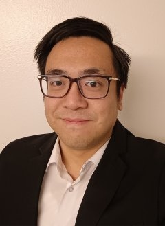 Man in black suit wearing glasses with short black hair.
