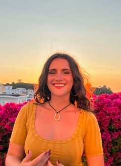 Woman wearing yellow top and black necklace with short wavy hair.