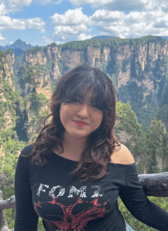 Woman in black top with long wavy black hair posing in front of mountain view point.
