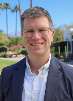 Man wearing navy colored suit with glasses and short brown hair.