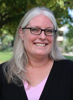 Woman wearing black and pink blouse with glasses and white long hair.