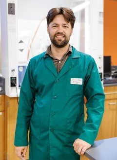 Man wearing dark green lab coat with brown short hair.