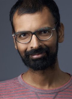 Man with short black hair wearing black glasses and red t-shirt.
