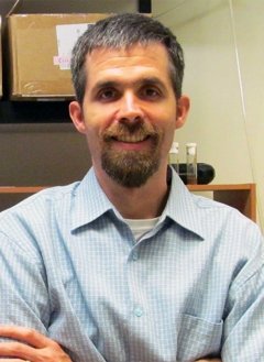 Man wearing light bluje button up with short grey hair.