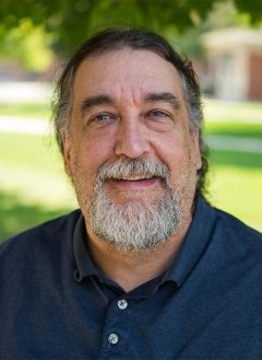 Man with white and brown beard wearing navy button up shirt.