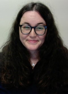 Woman with long black curly hair wearing glasses and black top.
