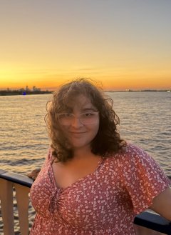 a girl with glasses standing with her back to the sunset over water