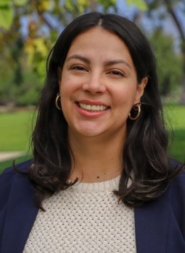 Closeup of Veronica Vriesman, who has long wavy dark hair and wears a blue blazer over a white knitted sweater.