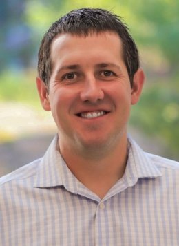 Closeup of Zachary Wilson, who has short dark hair and wears a plaid white and pale blue collared shirt.