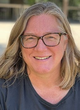 a woman with shoulder-legnth blond hair wears black glasses ad a blue tshirt