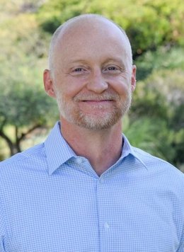 portrait of Brad Tharpe in front of trees wearing a blue collared shirt